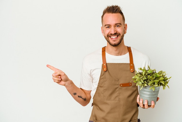 Jonge tuinman getatoeëerde blanke man met een plant geïsoleerd op een witte achtergrond glimlachend en opzij wijzend, iets laten zien op lege ruimte.