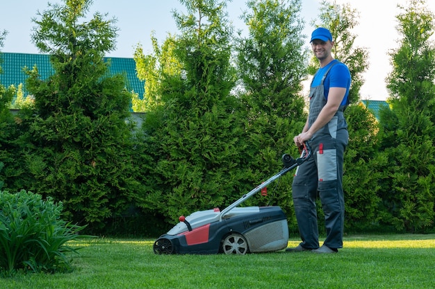 Jonge tuinman in overall gebruikt een grasmaaier op het perceel