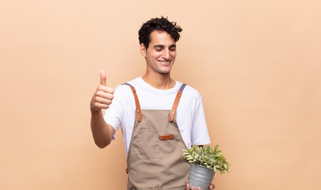 Jonge tuinman man trots, zorgeloos, zelfverzekerd en gelukkig, positief glimlachend met duimen omhoog