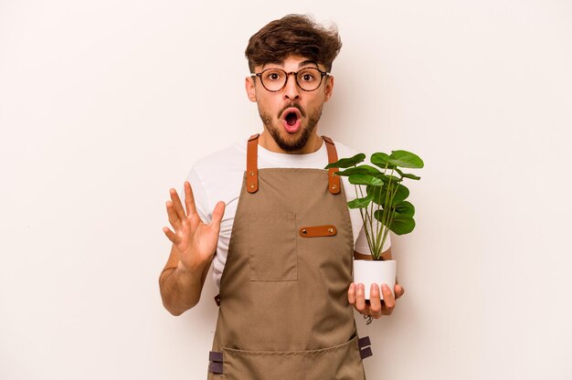 Jonge tuinman Spaanse man met een plant geïsoleerd op een witte achtergrond verrast en geschokt