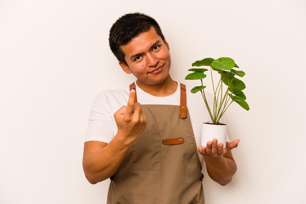 Jonge tuinman Spaanse man met een plant geïsoleerd op een witte achtergrond wijzend met de vinger naar je alsof uitnodigend dichterbij komen