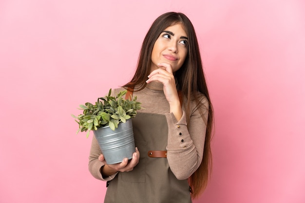 Jonge tuinman vrouw met een plant geïsoleerd op roze muur en opzoeken