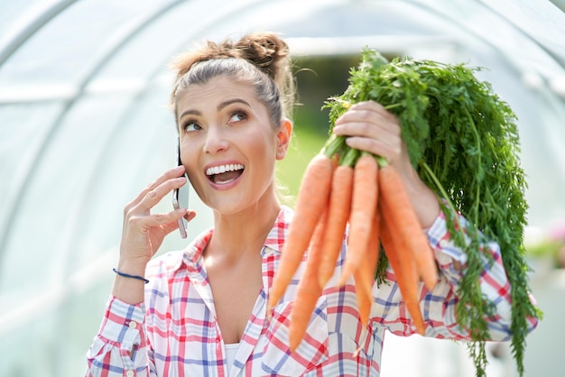 Jonge tuinmanvrouw met wortelen in serre