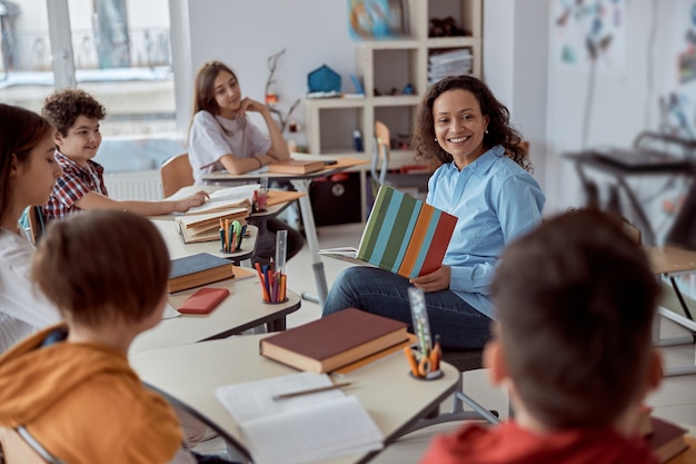 Jonge tutor leert haar student te lezen. Basisschoolkinderen zittend op een bureau en het lezen van boeken in de klas.