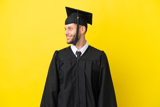 Jonge universitair afgestudeerde blanke man geïsoleerd op gele achtergrond op zoek naar kant
