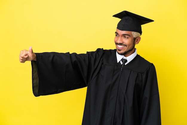 Jonge, universitair afgestudeerde Colombiaanse man geïsoleerd op een gele achtergrond met een duim omhoog gebaar