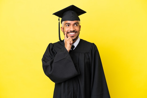 Jonge, universitair afgestudeerde Colombiaanse man geïsoleerd op gele achtergrond die een idee denkt terwijl hij omhoog kijkt