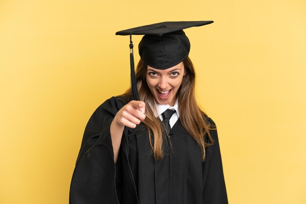 Jonge universitair afgestudeerde geïsoleerd op gele achtergrond verrast en wijzend naar voren