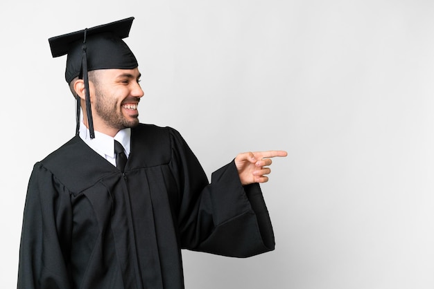 Jonge universitair afgestudeerde man over geïsoleerde witte achtergrond wijzende vinger naar de zijkant en een product presenteren