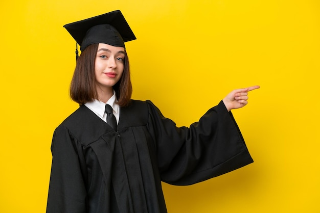 Jonge universitair afgestudeerde Oekraïense vrouw geïsoleerd op gele achtergrond wijzende vinger naar de zijkant