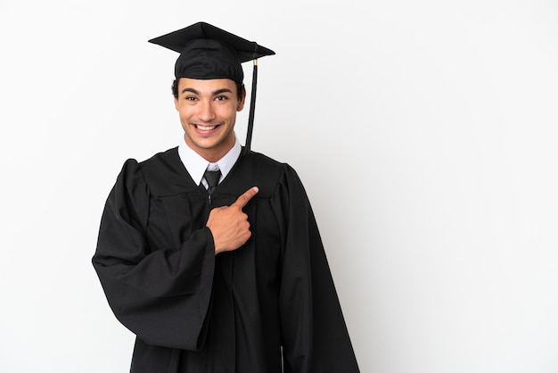 Jonge universitair afgestudeerde over geïsoleerde witte achtergrond wijzend naar de zijkant om een product te presenteren