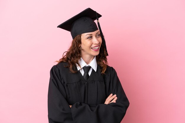 Jonge universitair afgestudeerde vrouw geïsoleerd op roze achtergrond gelukkig en lachend
