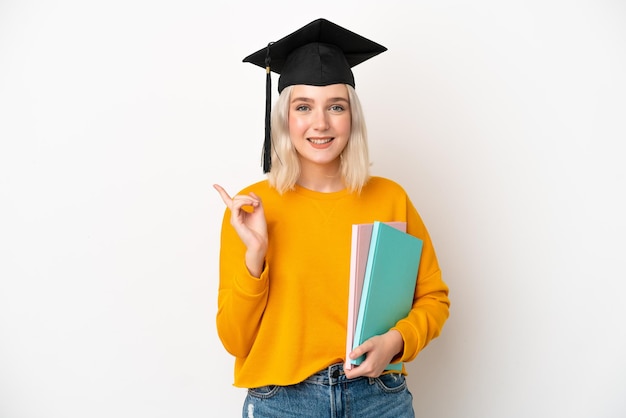 Jonge universitaire blanke vrouw afgestudeerd geïsoleerd op een witte achtergrond wijzend naar de zijkant om een product te presenteren