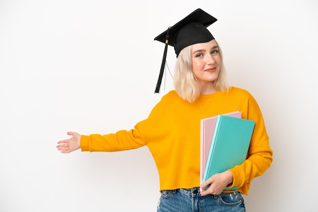 Jonge universitaire kaukasische vrouw afgestudeerd geïsoleerd op een witte achtergrond die de handen naar de zijkant uitstrekt om uit te nodigen om te komen