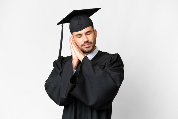 Jonge universiteitsgediplomeerde man over geïsoleerde witte achtergrond die slaapgebaar maakt in dorabele uitdrukking