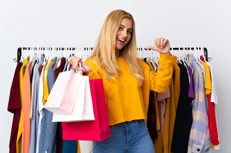 Foto jonge uruguayaanse blonde vrouw in een kledingwinkel en met boodschappentassen trots en zelfvoldaan