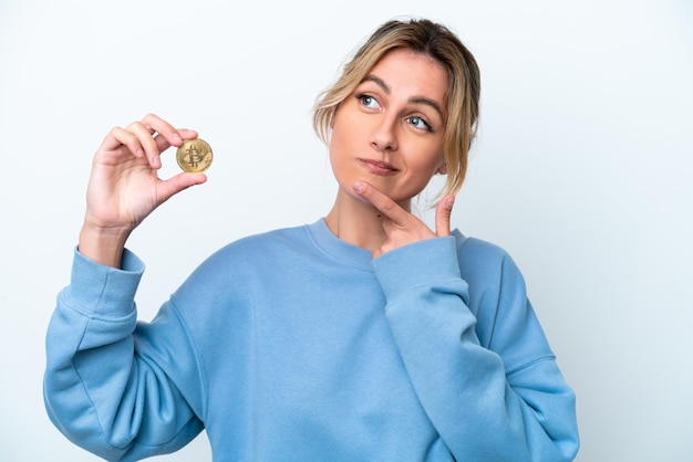 Jonge Uruguayaanse vrouw die een Bitcoin houdt die op witte achtergrond wordt geïsoleerd en omhoog kijkt