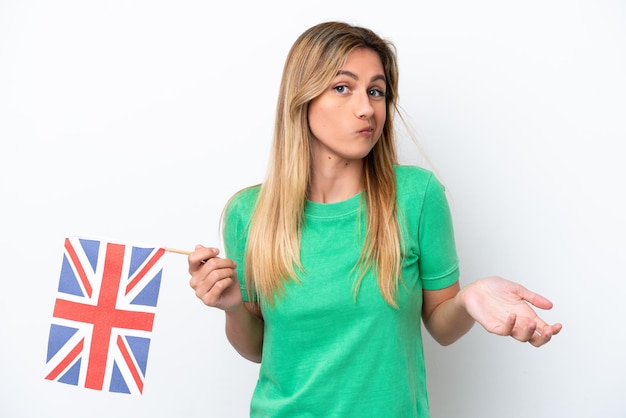 Jonge Uruguayaanse vrouw die een vlag van het Verenigd Koninkrijk vasthoudt die op een witte achtergrond wordt geïsoleerd en twijfels gebaar maakt terwijl ze de schouders opheft