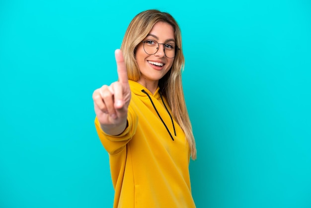 Jonge Uruguayaanse vrouw die op blauwe achtergrond wordt geïsoleerd die en een vinger toont opheft