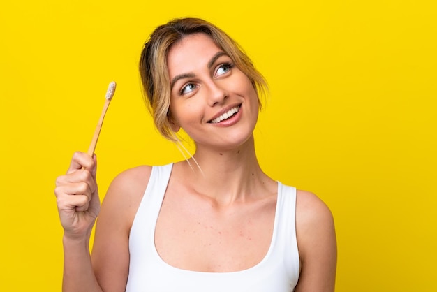 Jonge Uruguayaanse vrouw die tanden poetst geïsoleerd op gele achtergrond terwijl ze glimlacht