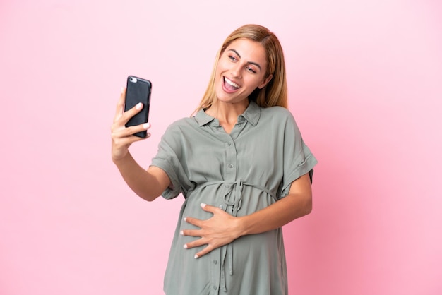 Jonge Uruguayaanse vrouw geïsoleerd op blauwe achtergrond zwanger en het maken van een selfie