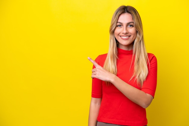 Jonge Uruguayaanse vrouw geïsoleerd op een gele achtergrond die naar de zijkant wijst om een product te presenteren