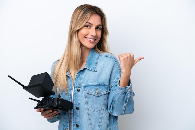 Jonge Uruguayaanse vrouw met een drone-afstandsbediening geïsoleerd op een witte achtergrond die naar de zijkant wijst om een product te presenteren
