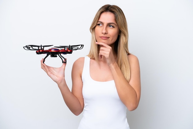 Jonge Uruguayaanse vrouw met een drone die op een witte achtergrond wordt geïsoleerd en twijfelt en denkt