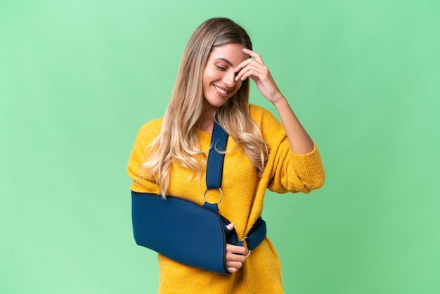 Jonge Uruguayaanse vrouw met gebroken arm en draagt een mitella over geïsoleerde lachende achtergrond