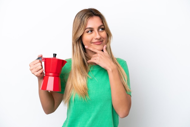 Jonge Uruguayaanse vrouw met koffiepot geïsoleerd op een witte achtergrond die een idee denkt en naar de kant kijkt