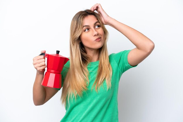 Jonge Uruguayaanse vrouw met koffiepot geïsoleerd op een witte achtergrond met twijfels en met verwarde gezichtsuitdrukking