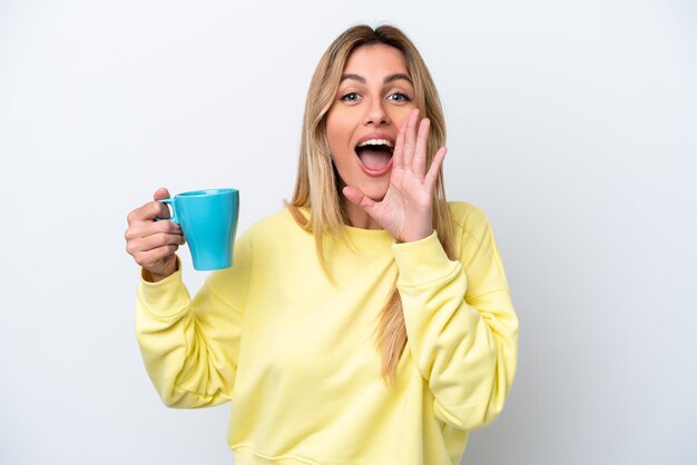 Jonge Uruguayaanse vrouw met kopje koffie geïsoleerd op een witte achtergrond schreeuwend met wijd open mond