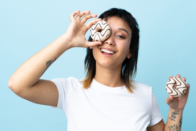 Jonge Uruguayaanse vrouw over blauwe muur die een doughnut en gelukkig houdt