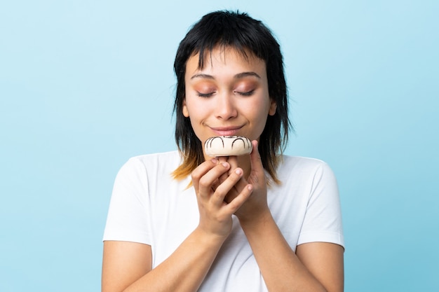 Jonge Uruguayaanse vrouw over geïsoleerd blauw dat een doughnut houdt
