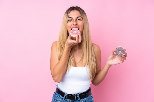 Jonge Uruguayaanse vrouw over geïsoleerde roze muur die een doughnut eet