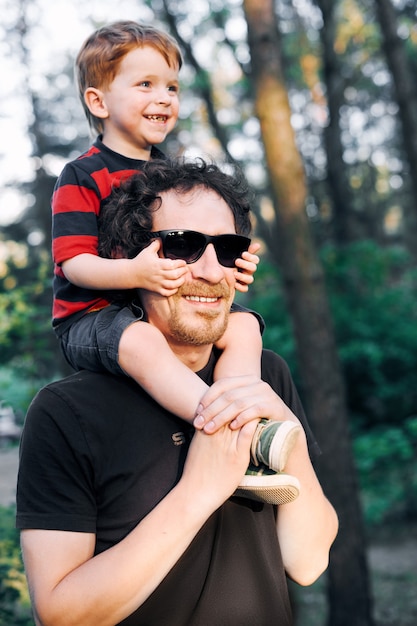 Jonge vader die in de zomer met zijn jonge zoon in het park loopt en het op zijn schouders houdt