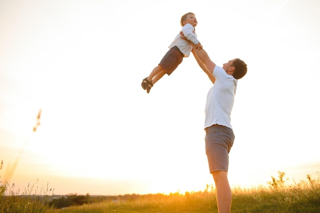 Jonge vader gooit zijn schattige en kleine zoon over in de frisse lucht Vaderdag Vader en zijn zoon babyjongen buiten spelen en knuffelen