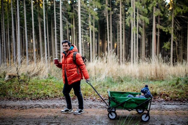 Jonge vader loopt met een kind in een wagen in het bos