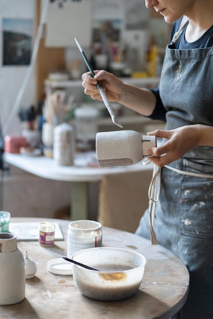 Jonge vakvrouw schildert vaas met penseel na het bakken en handgemaakte vormgeving in studio