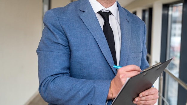 Jonge veelbelovende man in een klassiek pak met een tabletband in zijn handen en geld staat in de gang van het kantoor Bedrijfs- en winstconcept