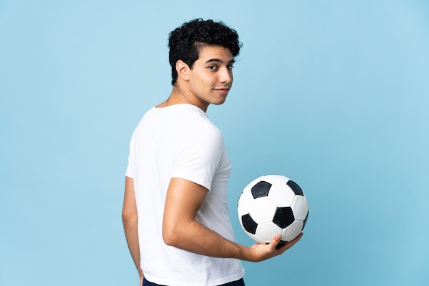 Jonge Venezolaanse man geïsoleerd op blauwe muur met voetbal