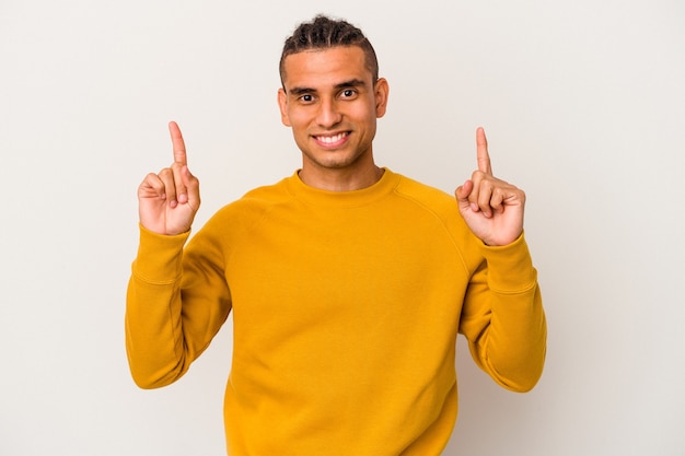 Jonge Venezolaanse man geïsoleerd op een witte achtergrond geeft aan met beide voorvingers omhoog met een lege ruimte.