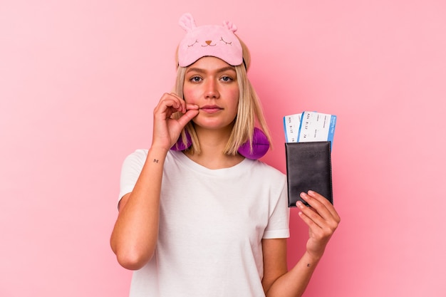 Jonge venezolaanse reizigersvrouw die een paspoort houdt dat op roze muur met vingers op lippen wordt geïsoleerd die een geheim bewaren.