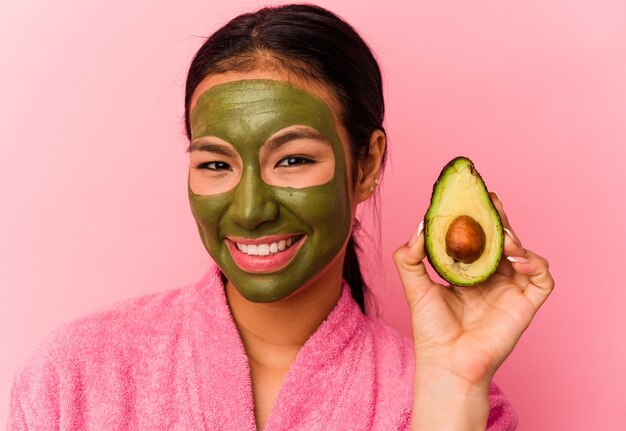 Jonge Venezolaanse vrouw die een gezichtsmasker draagt dat op roze achtergrond wordt geïsoleerd