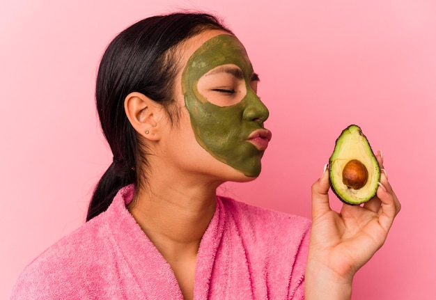 Jonge Venezolaanse vrouw die een gezichtsmasker draagt dat op roze achtergrond wordt geïsoleerd