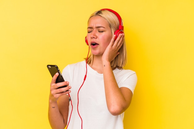 Jonge Venezolaanse vrouw die muziek luistert die op gele achtergrond wordt geïsoleerd