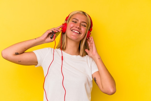 Jonge Venezolaanse vrouw die muziek luistert die op gele achtergrond wordt geïsoleerd