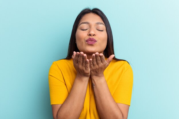 Jonge venezolaanse vrouw geïsoleerd op blauwe achtergrond die lippen vouwt en handpalmen vasthoudt om luchtkus te sturen.