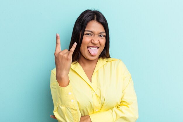 Jonge Venezolaanse vrouw geïsoleerd op blauwe achtergrond met rock gebaar met vingers