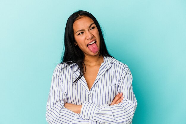 Jonge Venezolaanse vrouw geïsoleerd op blauwe muur grappig en vriendelijk tong uitsteekt.